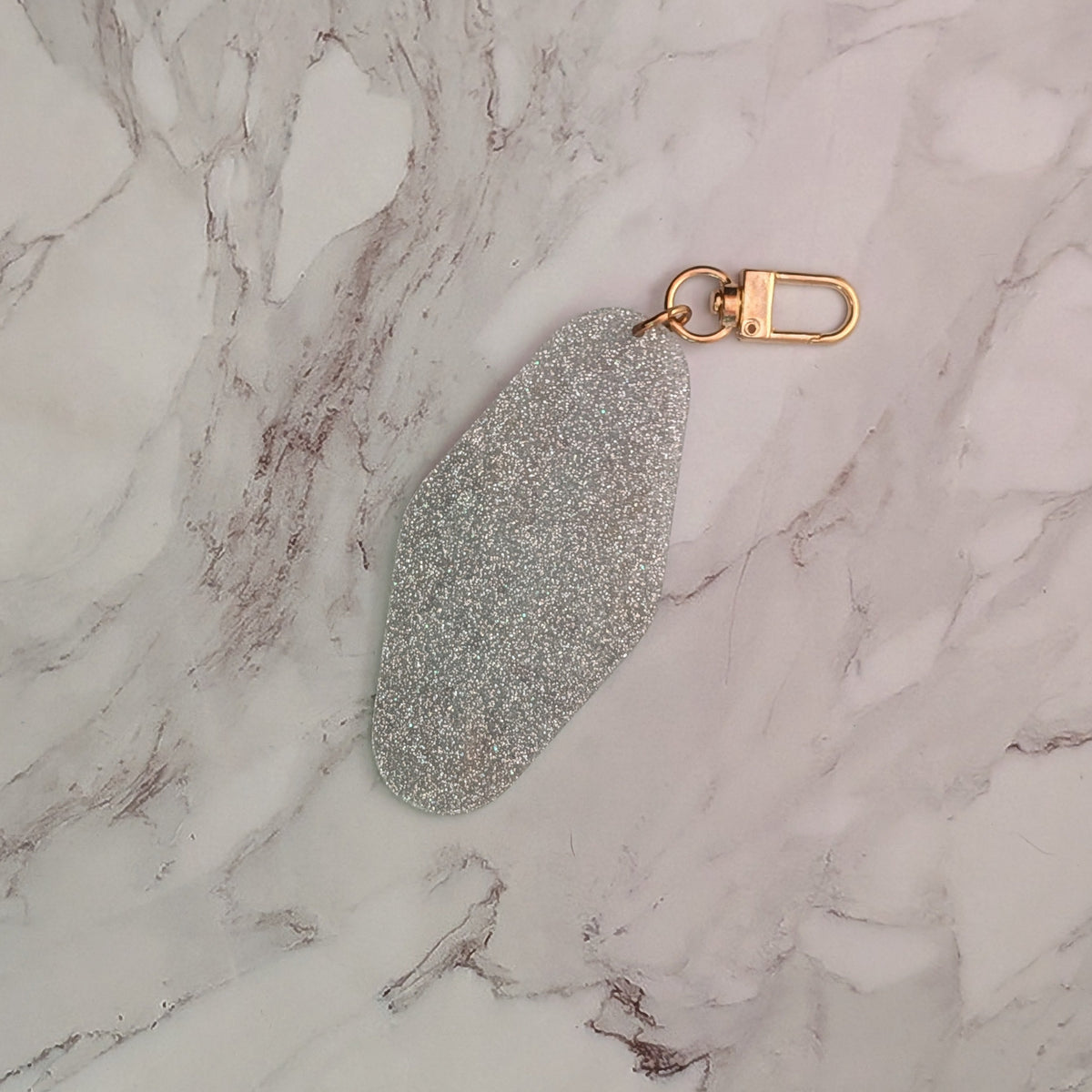 A silver glitter keychain with a gold-tone lobster clasp, resting on a white and gray marble surface.