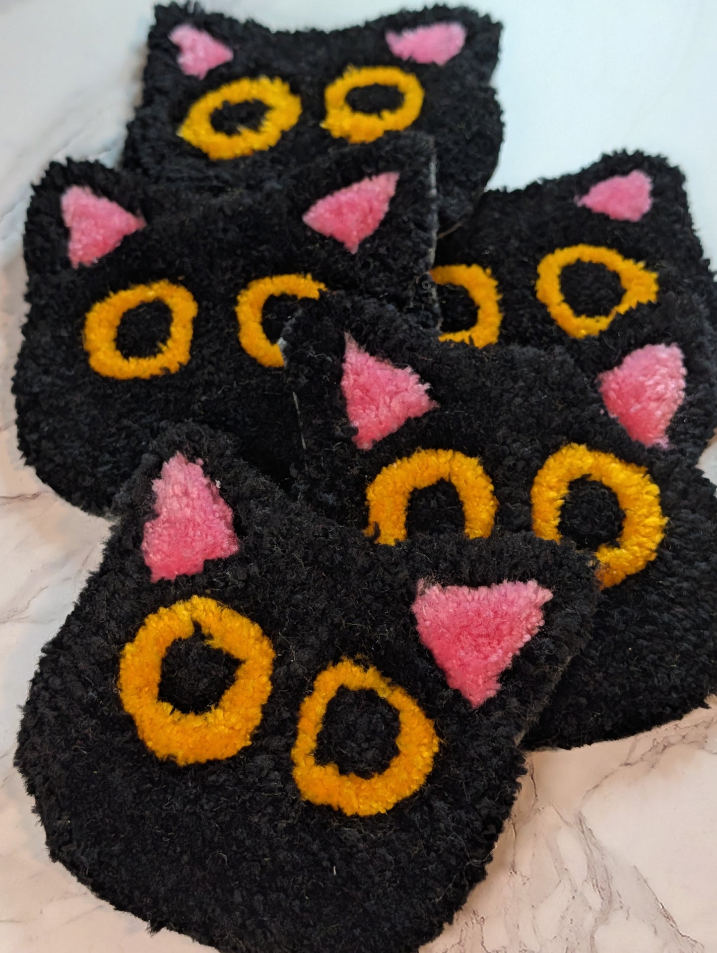 several Black cat-shaped tufted mug rug with pink ears and yellow eyes on a marble background