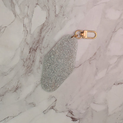 A silver glitter keychain with a gold-tone lobster clasp, resting on a white and gray marble surface.