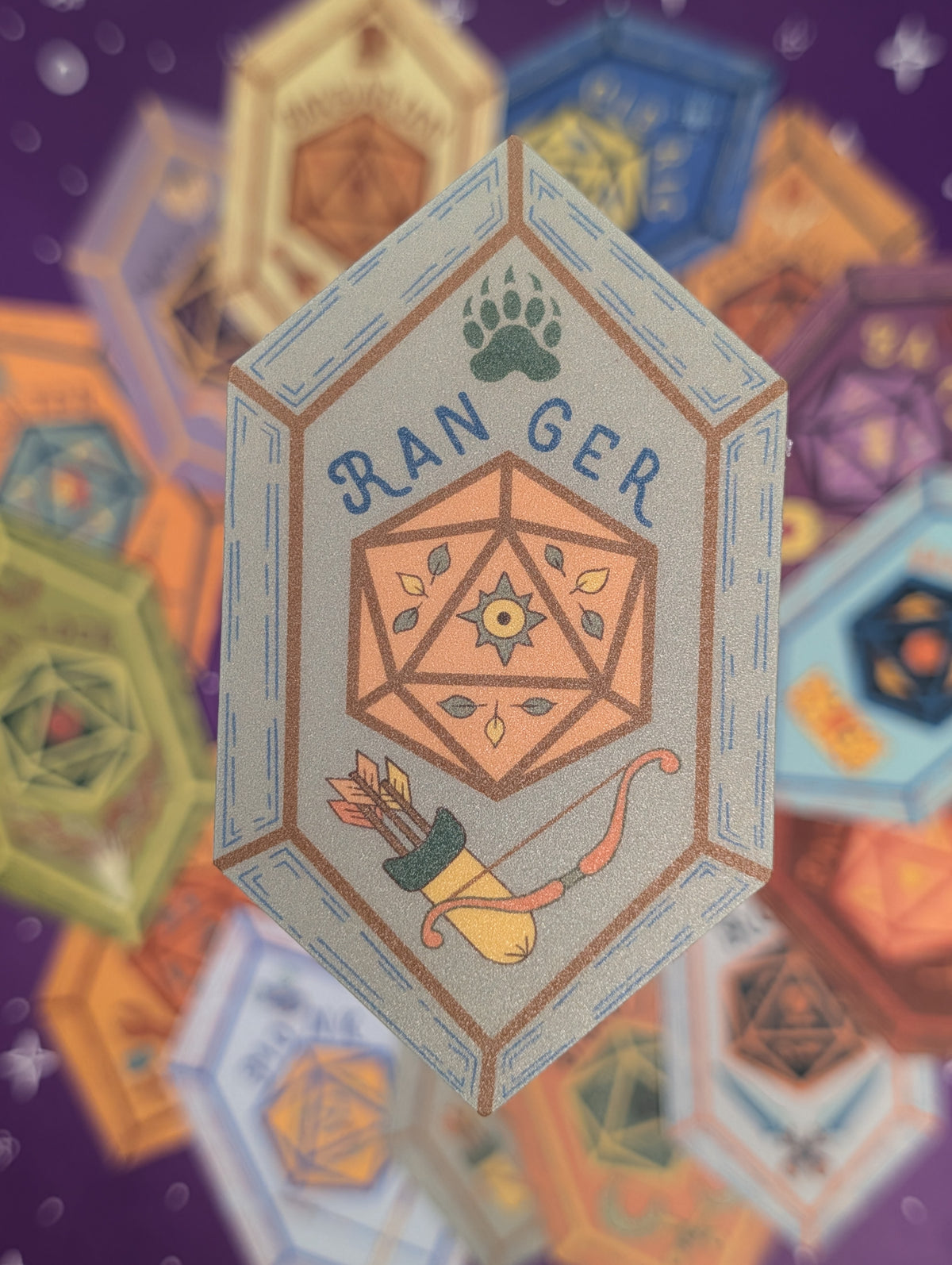 A centered illustrated hexagonal sticker reading "D20 RANGER" with a paw print, geometric emblem, and bow and arrow, surrounded by blurred multicolored polyhedral icons on a purple background.