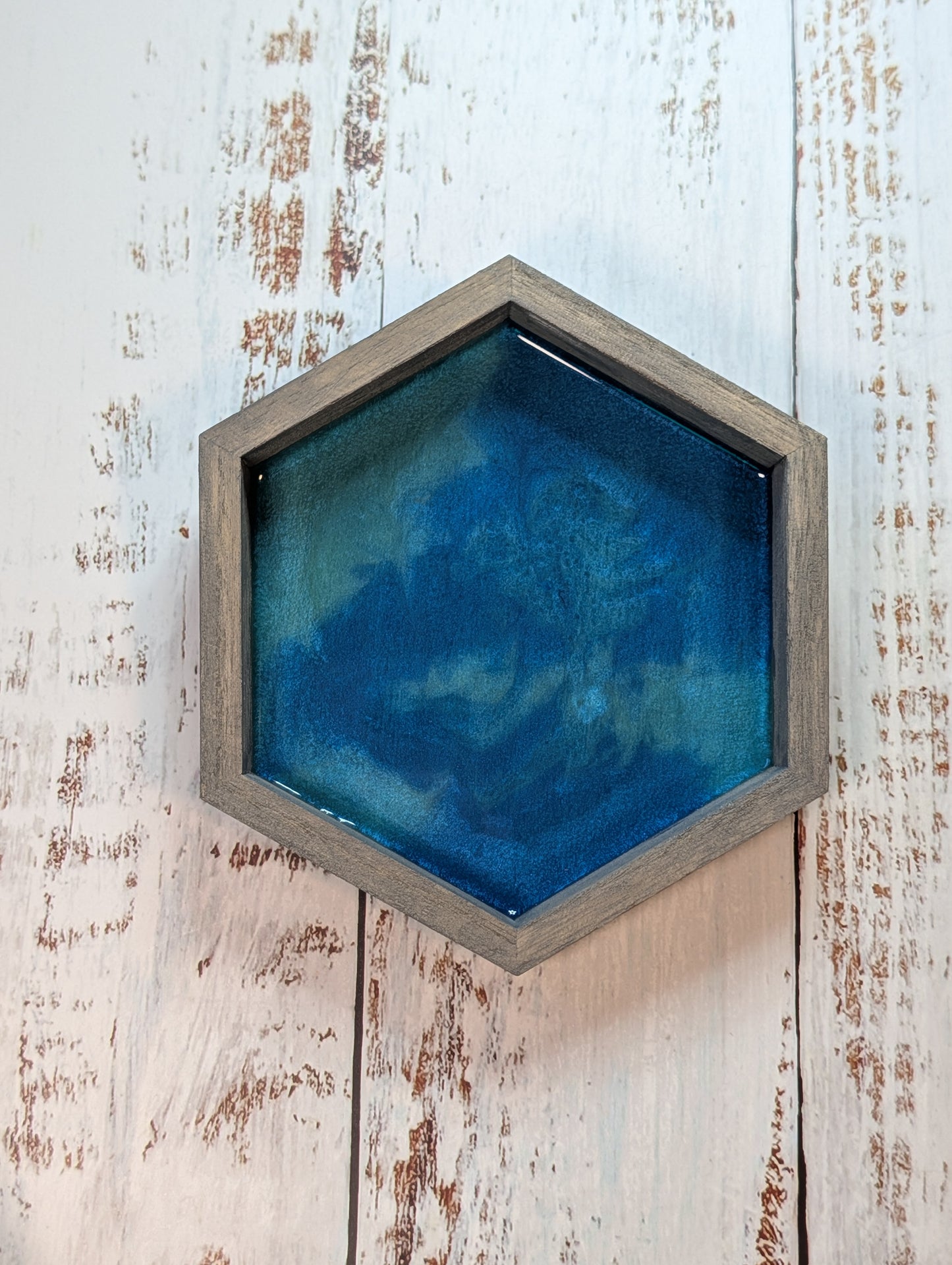 Hexagonal blue artwork in a wooden frame on a rustic wooden wall.